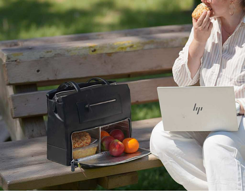 femme élégante travaillant sur son ordinateur et prenant son déjeuner depuis le compartiment isotherme du sac l'intemporel de haksam parisen cuir togo avec fruits, pizza et petite salade